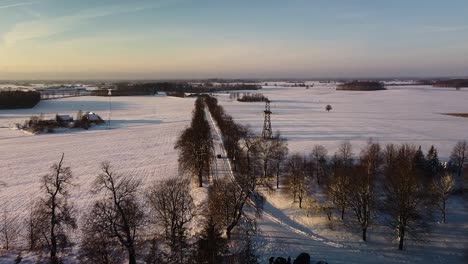 hermosa vista aérea de pájaro de campos cubiertos de nieve y carretera de grava rural en un día soleado de invierno, hora dorada, coche en la carretera, disparo de drone de gran ángulo avanzando