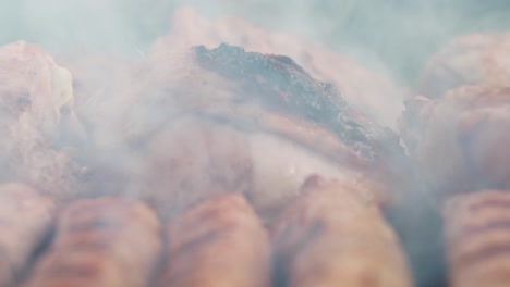with tongs, he turns the chicken thighs on the grill. in the smoke from the coals