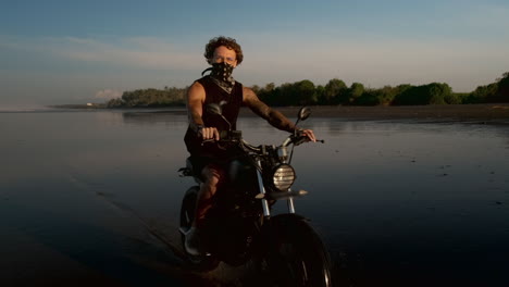 hombre montando una motocicleta en una playa de arena negra al atardecer
