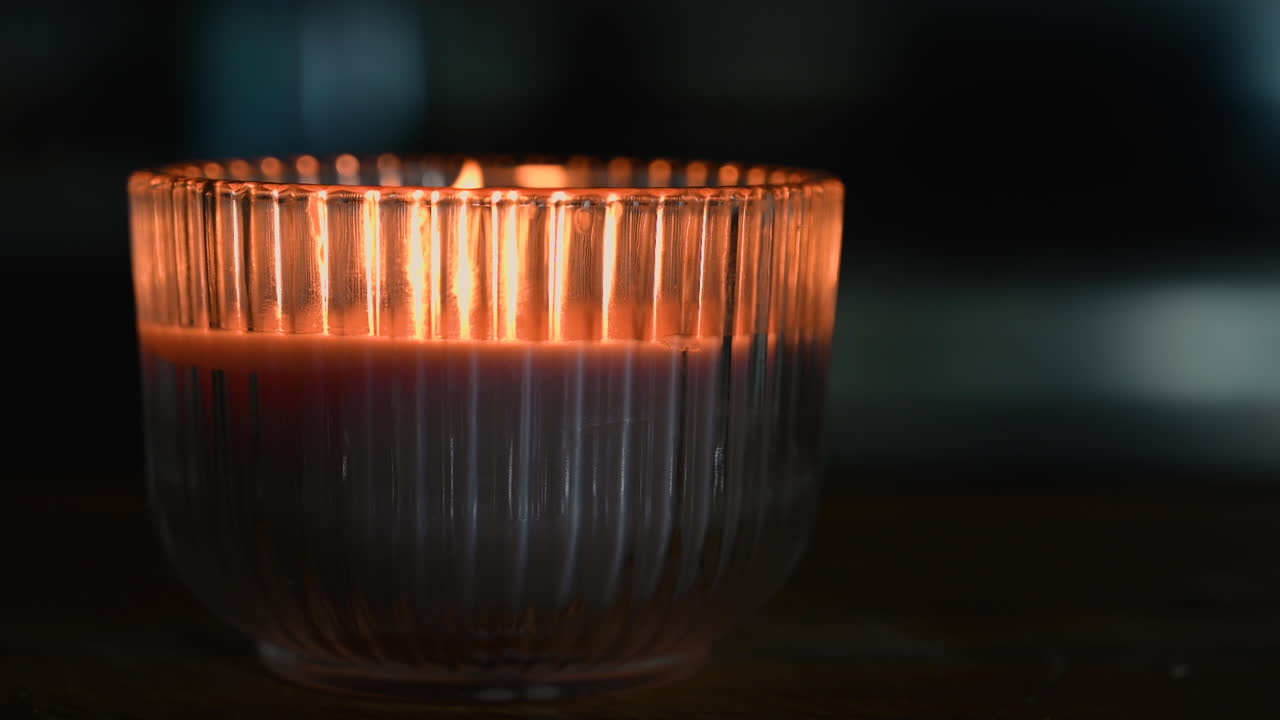 Burning candle in the glass cup, moving fire by wind blowing in the darkness