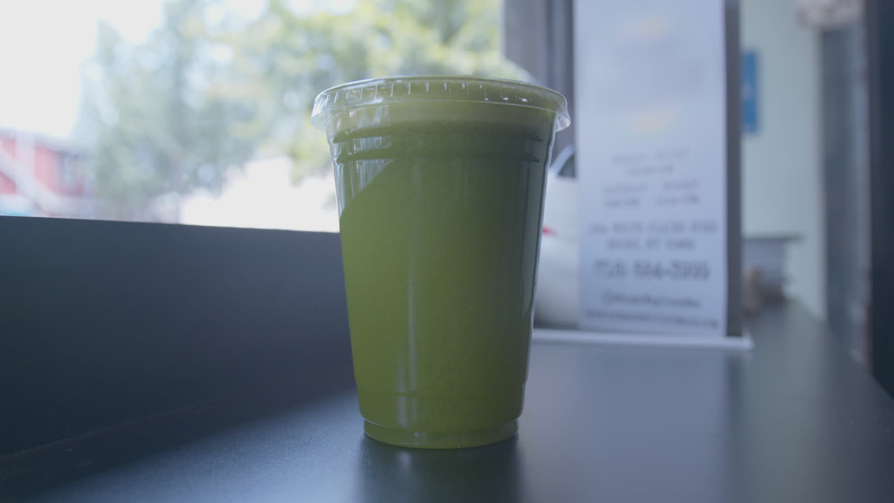 창문 근처의 컵에 녹색 주스의  ⁇ 리 앞을 닫으십시오