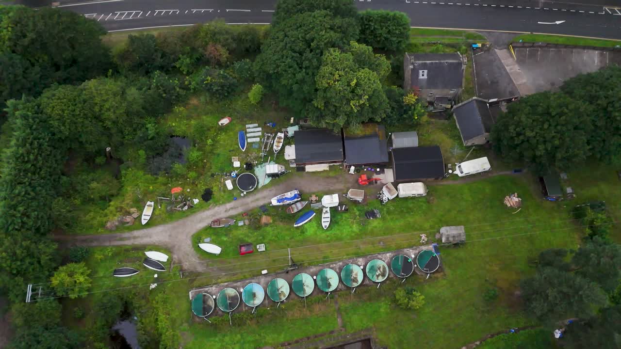 Drone footage ascends over a rural fish farm with circular tanks, green landscape, and nearby road, under soft daylight with steady camera movement