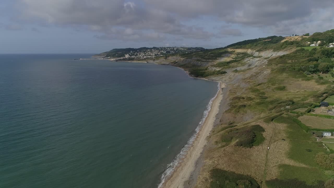 Aerial on the edge of Charmouth tracking forwards along the coast towards Lyme Regis