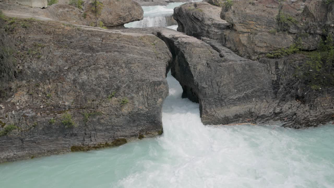 Blue water pouring through a shoot at the bottom of the Natural Bridge lower falls at Yoho National Park.