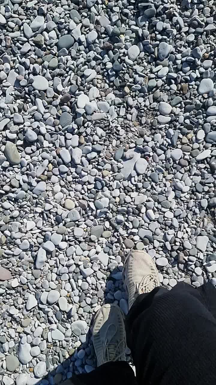VERTICAL Slow motion walking on white pebble stone beach wearing sports footwear