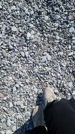 vertical slow motion walking on white pebble stone beach wearing sports footwear