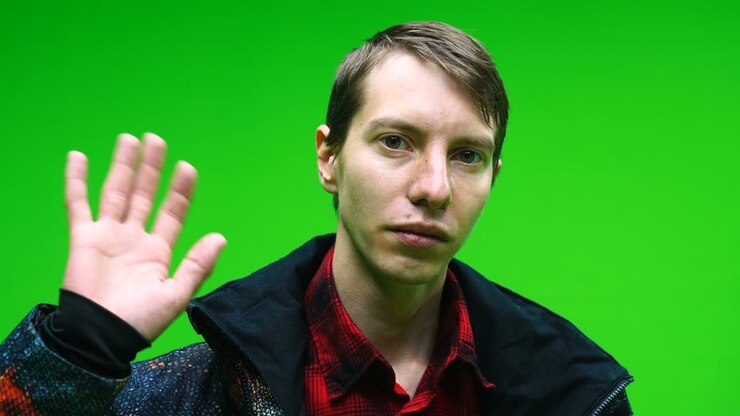 Giovane uomo in abiti casual che saluta con la mano su sfondo green screen.