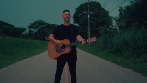 man playing acoustic guitar on a country road at dusk