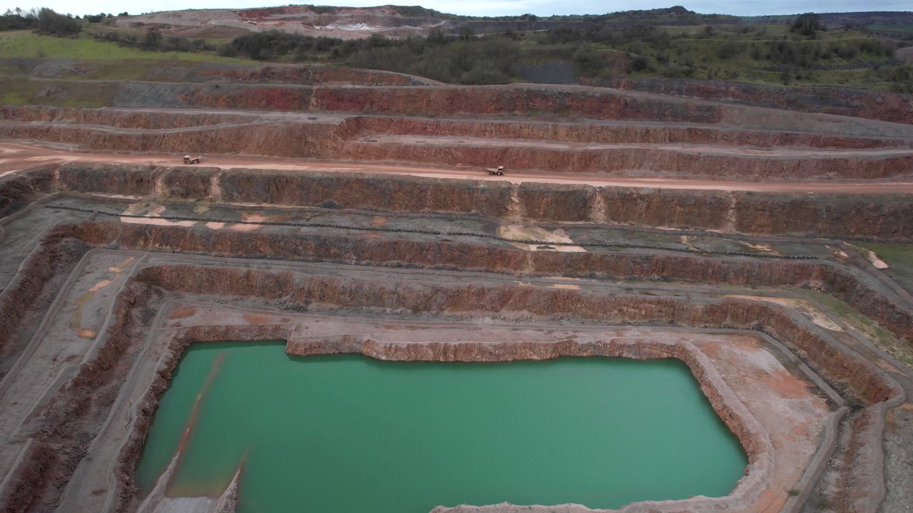 Aerial view of industrial quarry site with trucks and blue lagoon lake