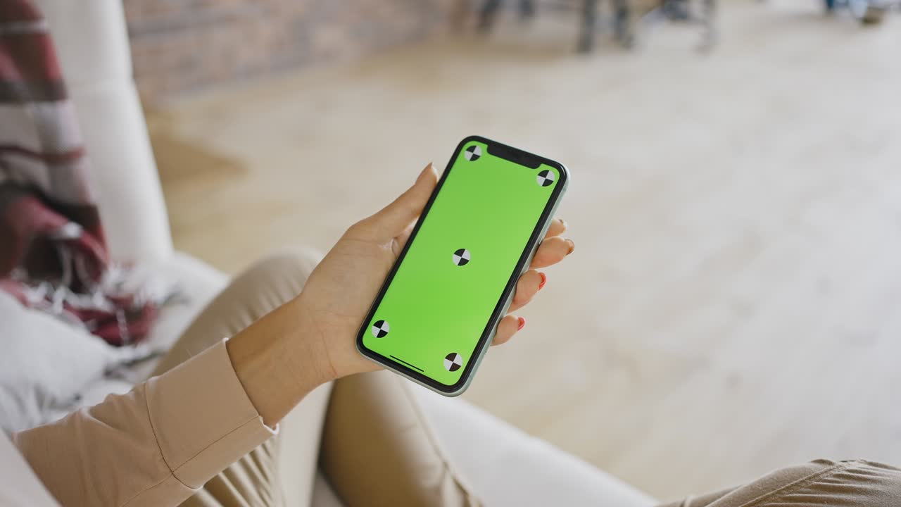 Close up woman sitting at home on the couch with a smartphone in her hands. Mobile phone greenscreen mock-up technology. Close-up girl using modern smartphone social life networking