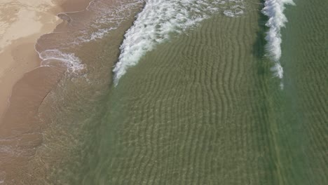 aerial static shot of small clear tropical ocean waves breaking on the white sand beach