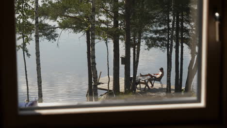 view outside window at lakehouse, man is reading and relaxing on the dock