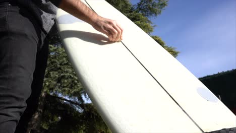 Vista-De-ángulo-Bajo-De-Un-Surfista-Encerando-La-Tabla-En-El-Jardín