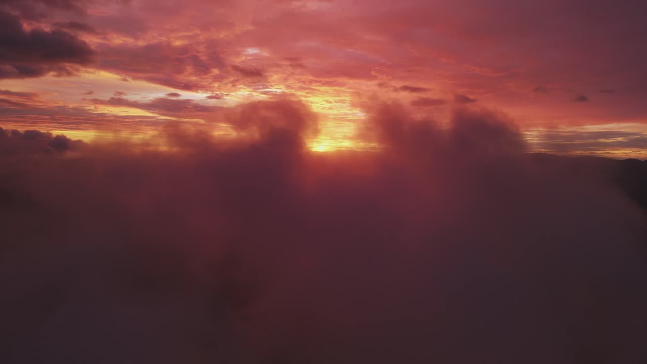Hellrote Sonne hinter nebligen Wolken am Himmel bei Sonnenuntergang, 4K Drohnenaufnahme.