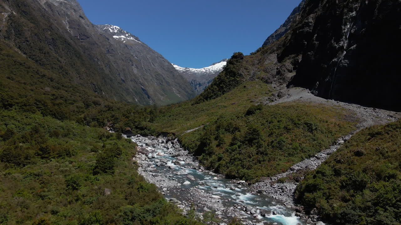río rápido de montaña en un estrecho valle rocoso debajo de los picos de las montañas en fiordland southland, nueva zelanda