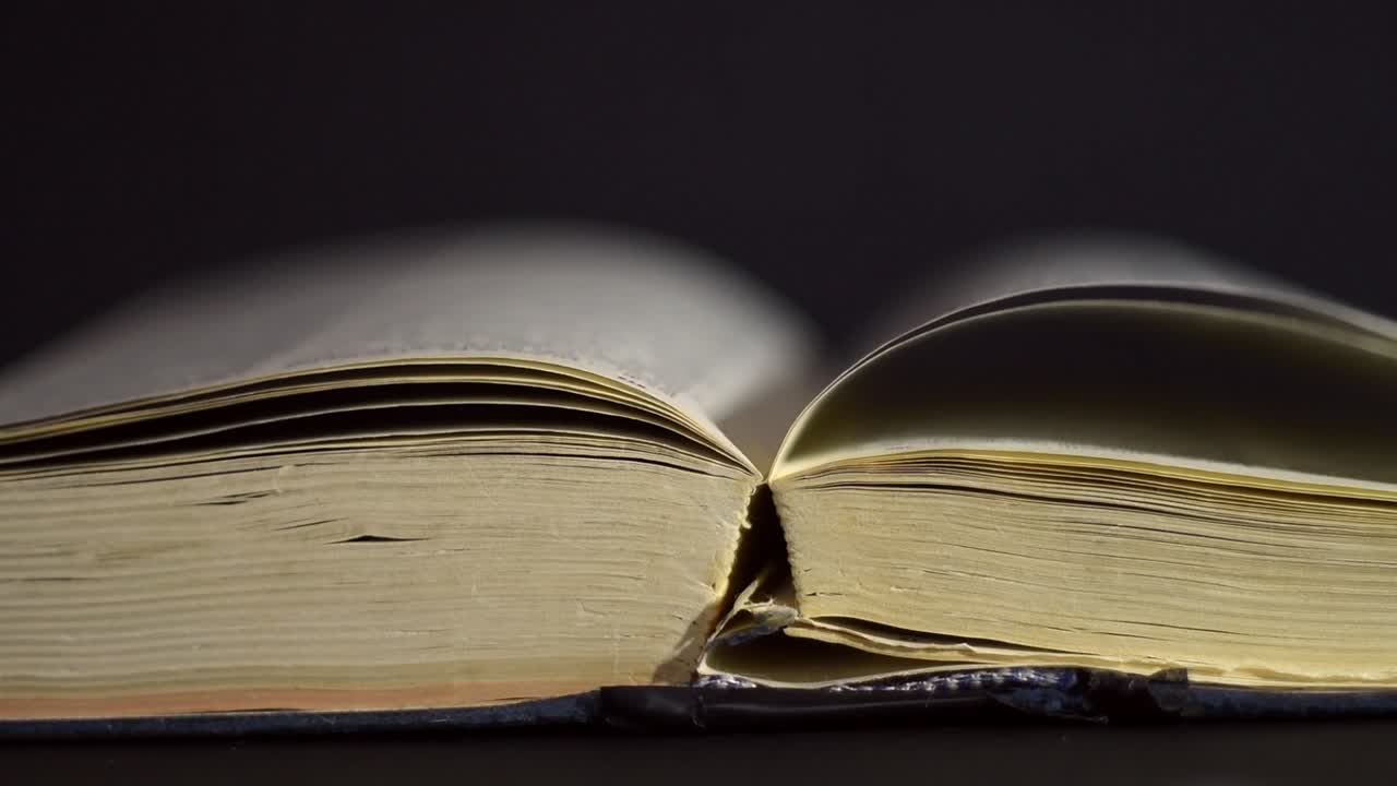 cámara lenta, primer plano de un libro antiguo, vintage, abierto con páginas girando en el viento, en una habitación oscura con poca luz, con un entorno negro