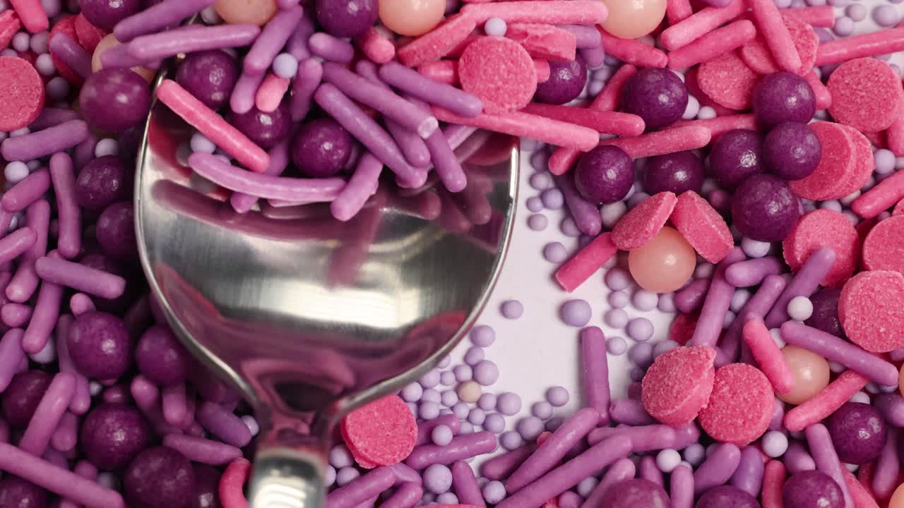 A close-up of vibrant pink and purple candies with a spoon stirring through them, highlighting texture and color contrast