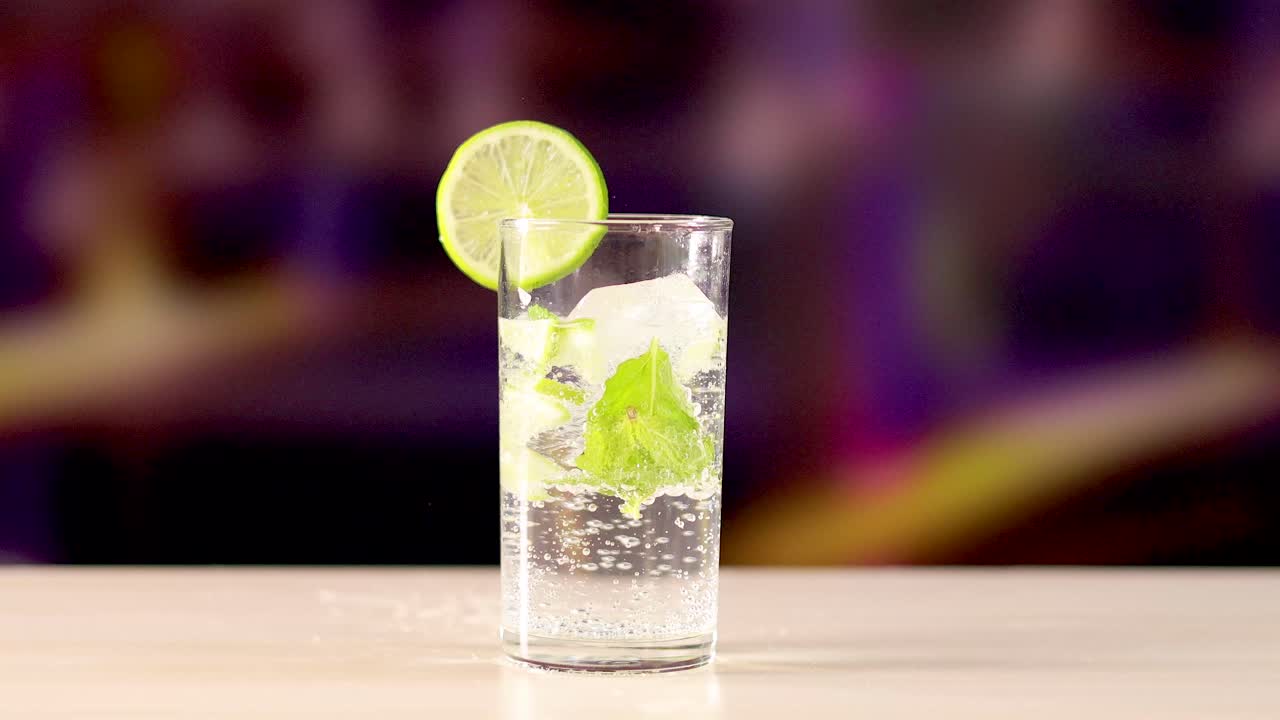 A mojito cocktail with lime and mint in a glass on a bar counter, set against a blurred colorful background