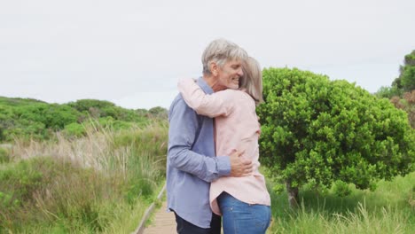 pareja caucásica mayor sonriente abrazándose y de pie en el camino al aire libre