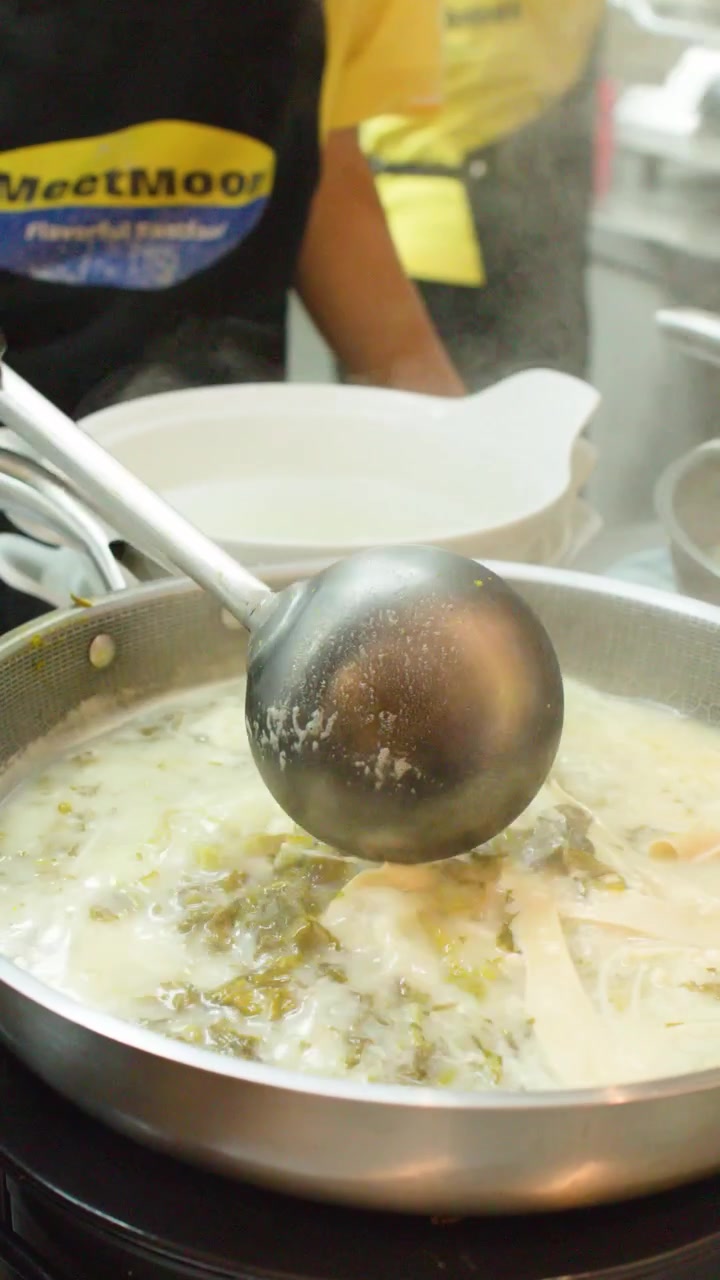 Close-up of a chef stirring steaming Asian soup in a wok using a large ladle.