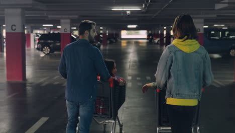 rear view of two caucasian man walking in a empty parking, talking and carrying their girlfriends in trolleys