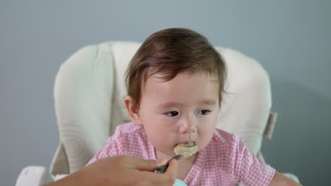 cute toddler girl eating oatmeal seated in high chair at home