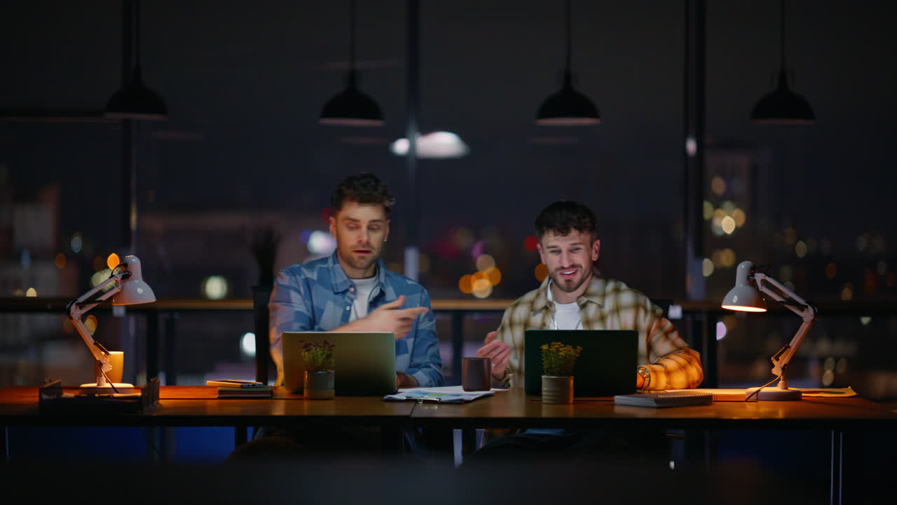 Design professionals working laptop shaking hands at dark office. Two developers