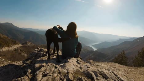 girl sitting and cudling black labrador dog on a mountain with beautiful lake canyon in the background