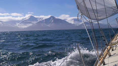 navegando un yate en el ártico con montañas nevadas - las olas chocan contra el casco en cámara lenta