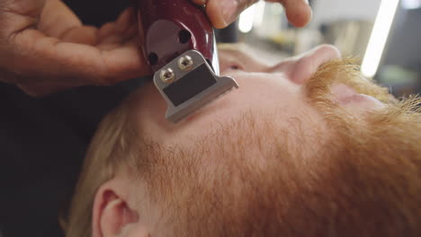 barbero dando forma a la barba del cliente con un cortador