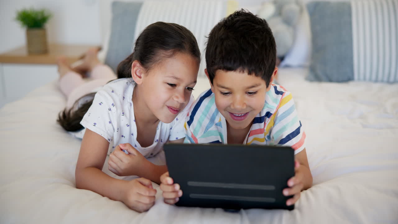 hermanos viendo la tableta en la cama