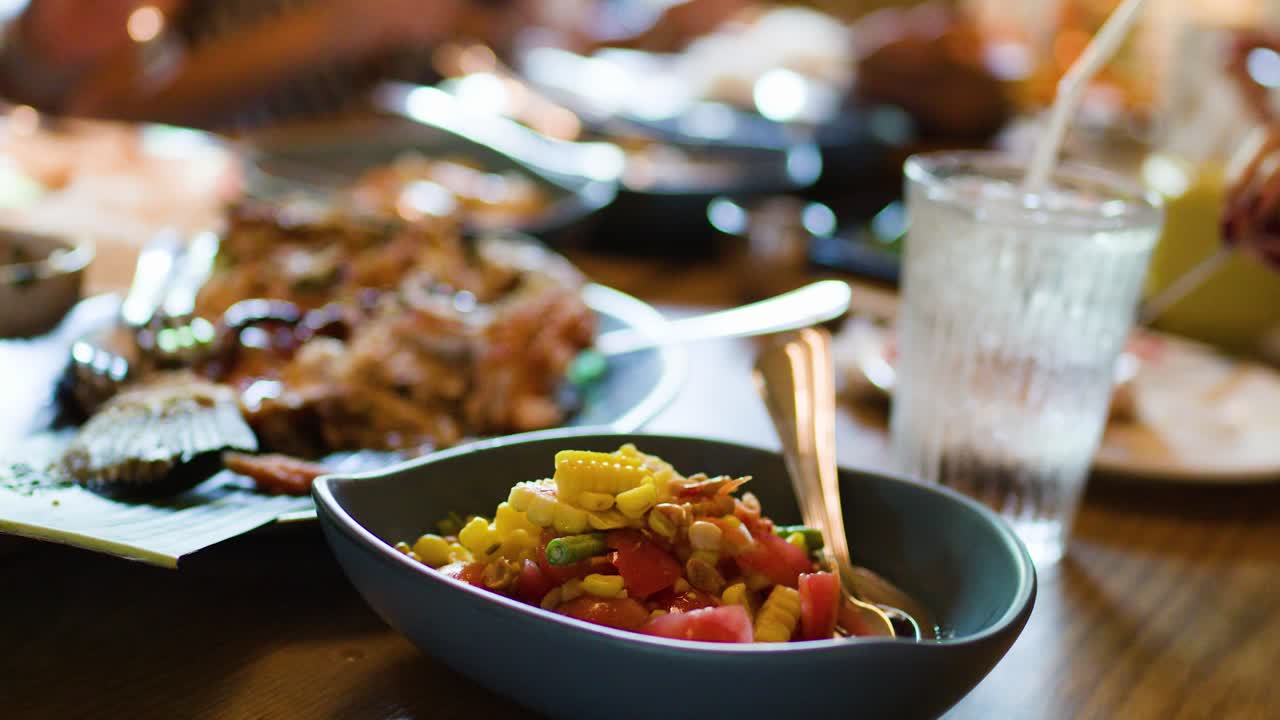 Close-up of colorful Thai corn salad, grilled fish, and greens on restaurant table, natural lighting