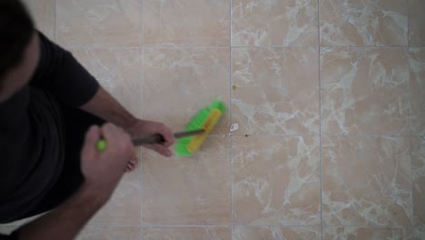 video from above of a bearded man sweeping his living room's floor with a black and green broom