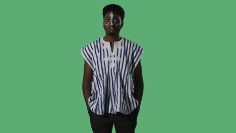 retrato de un joven afroamericano con una expresión sorprendida y sorprendida. hombre negro con un patrón étnico blanco en la cara y con camisa nacional a rayas posando en pantalla verde en el estudio