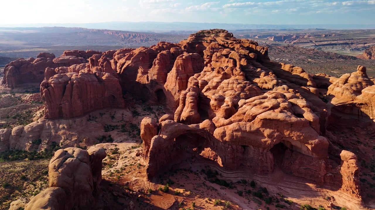 Splendido filmato stock del Parco Nazionale di Arches, USA, durante un pomeriggio luminoso. La luce solare brillante illumina le maestose strutture di arenaria rossa e il paesaggio desertico sotto un cielo azzurro limpido.
