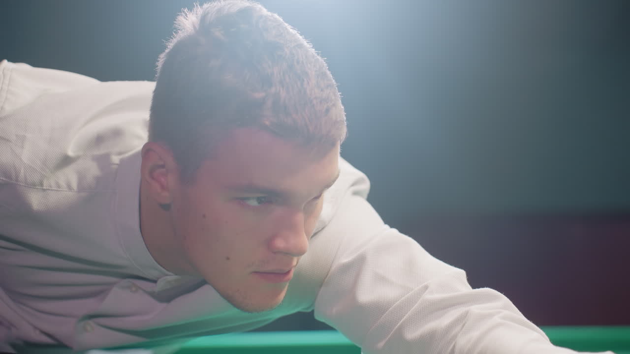 색 셔츠를 입은 게이머가 희미하게 조명된 방에서 초록색 빌리어드 테이블에 기대어, 강렬한 초점을 맞추는 큐 스틱을 잡고, 전략적인  설정, 정밀 플레이, 극적인 조명