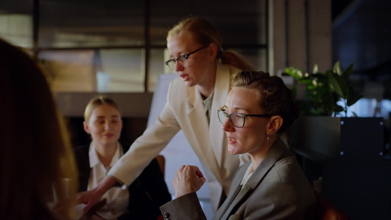 Side view of a confident middle-aged blonde girl in glasses and a business uniform talking with her colleagues during a meeting about work and a meeting in a modern office
