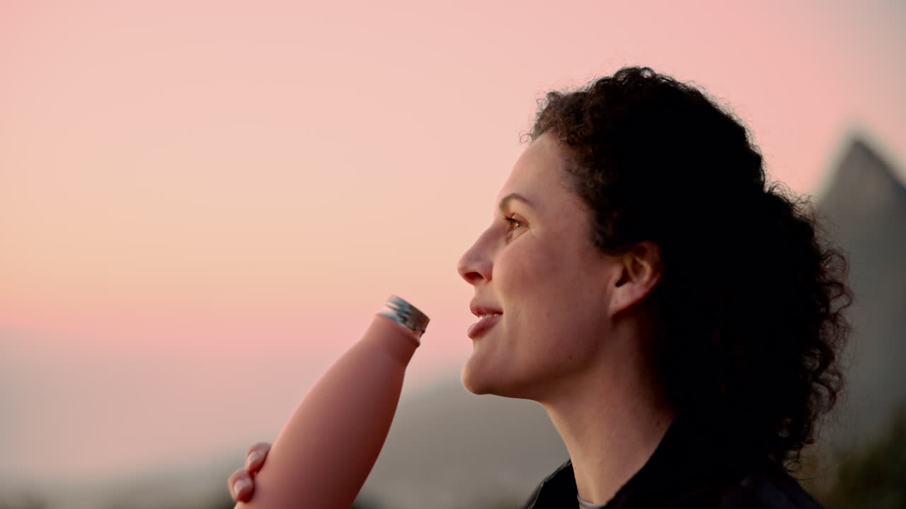 mujer bebiendo de una botella de agua reutilizable al atardecer