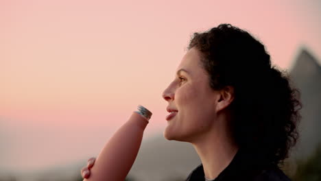 woman drinking from a reusable water bottle at sunset