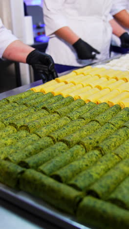 three cooks put the big trays with semi-cooked food on the metal table. stuffed pancakes and meat ravioli manufactured at food factory. vertical video