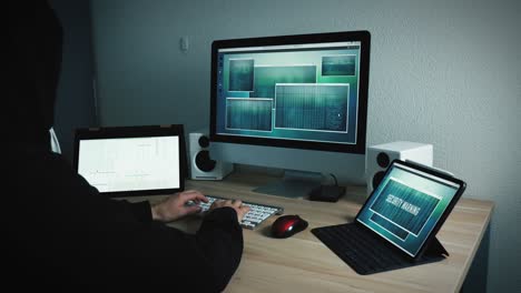 Unrecognizable hooded hacker programs a virus at his work place to gain access to other computers