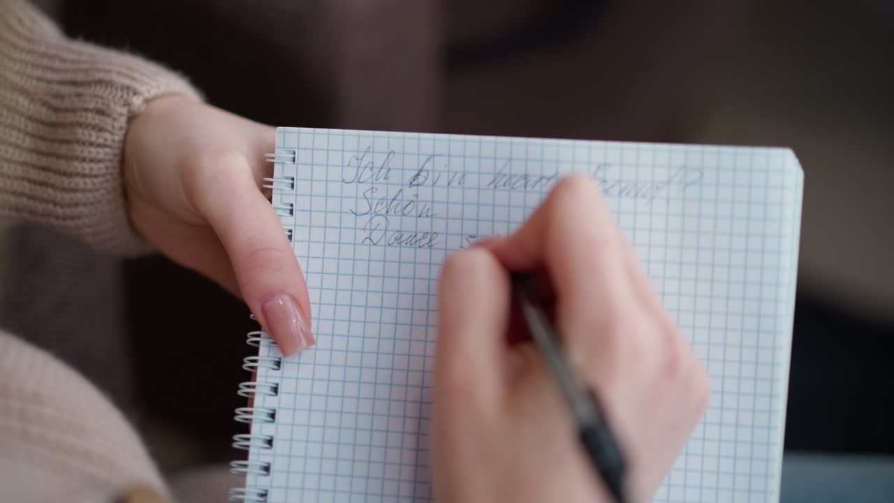 Close-up hand view of individual writing in notebook with pen, showing graceful hand movements on graph paper, capturing details of handwriting process