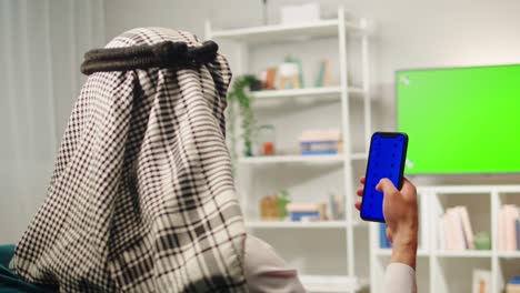arabic man using smartphone with blue screen while watching green screen tv