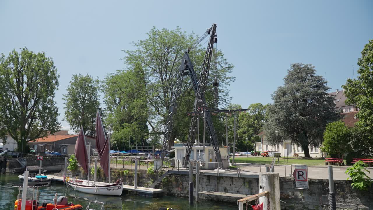 velero tradicional atracado por un río tranquilo con una grúa y vegetación en lindau, bodensee en un día soleado