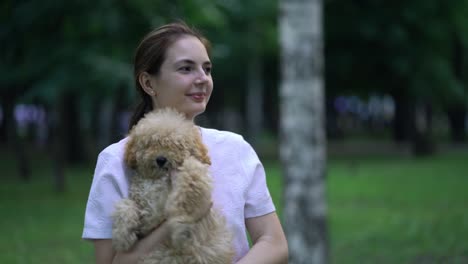 woman with toy poodle walking in a park.