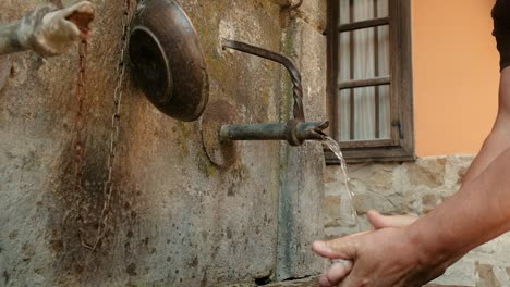 man washing hands under running cold spring water at an old village water supply fountain well