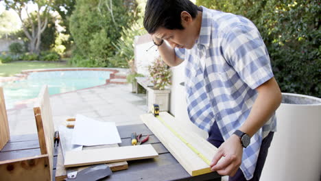 measuring wooden plank, asian man working on diy project in backyard workshop