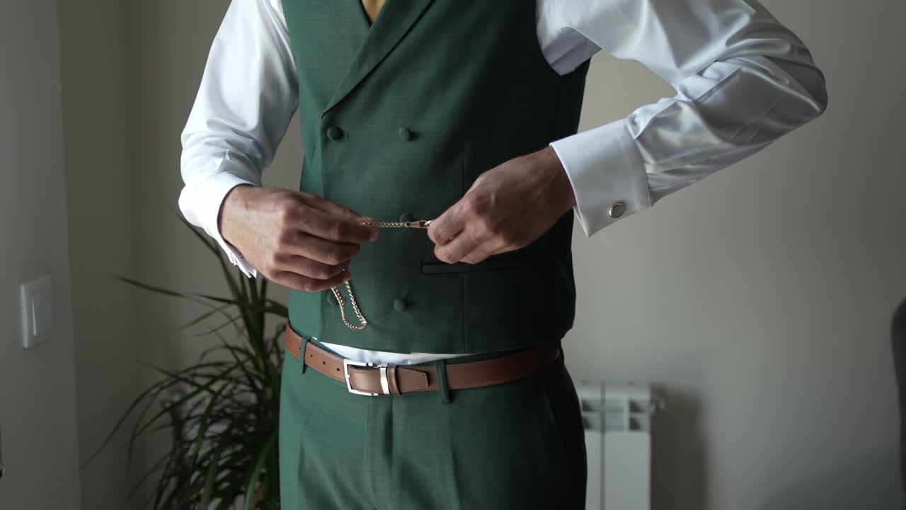 Man in a green vest and white shirt adjusting his outfit, featuring a pocket watch
