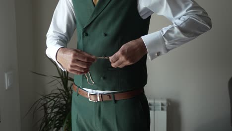 man in a green vest and white shirt adjusting his outfit, featuring a pocket watch