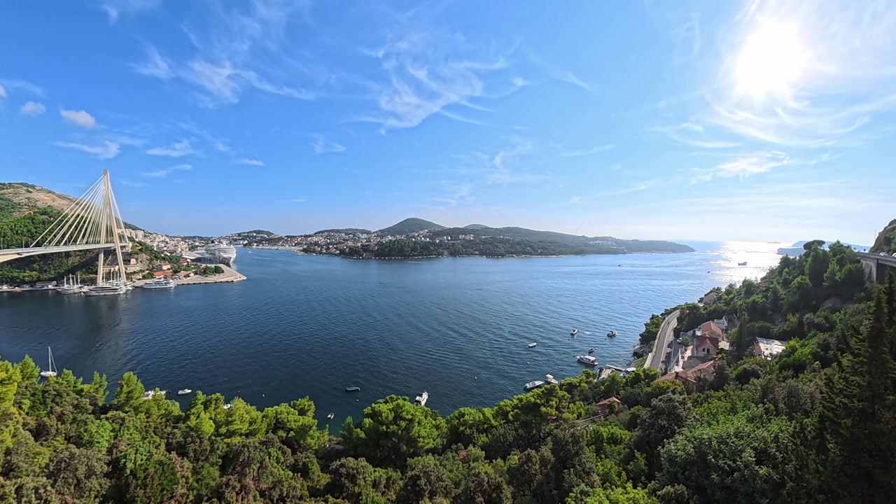 A stunning wide panoramic view over Gruž Port and the Dubrovnik Bridge in Croatia. The blue Adriatic Sea glistens under a clear sunny sky with boats and cruise ships in view.